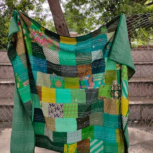 Könnte beinhalten: Ein Patchwork-Quilt in Grüntönen mit einer Vielzahl von Mustern und Texturen. Der Quilt besteht aus Stoffquadraten, die mit weißem Faden zusammengenäht sind. Der Quilt ist über einen Ast drapiert.