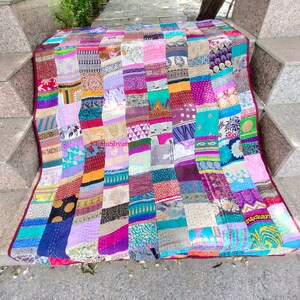 May include: A colorful patchwork quilt made from repurposed fabric scraps. The quilt is made up of squares of different colors and patterns, including floral, paisley, and geometric designs. The quilt is laid out on a set of stone steps.