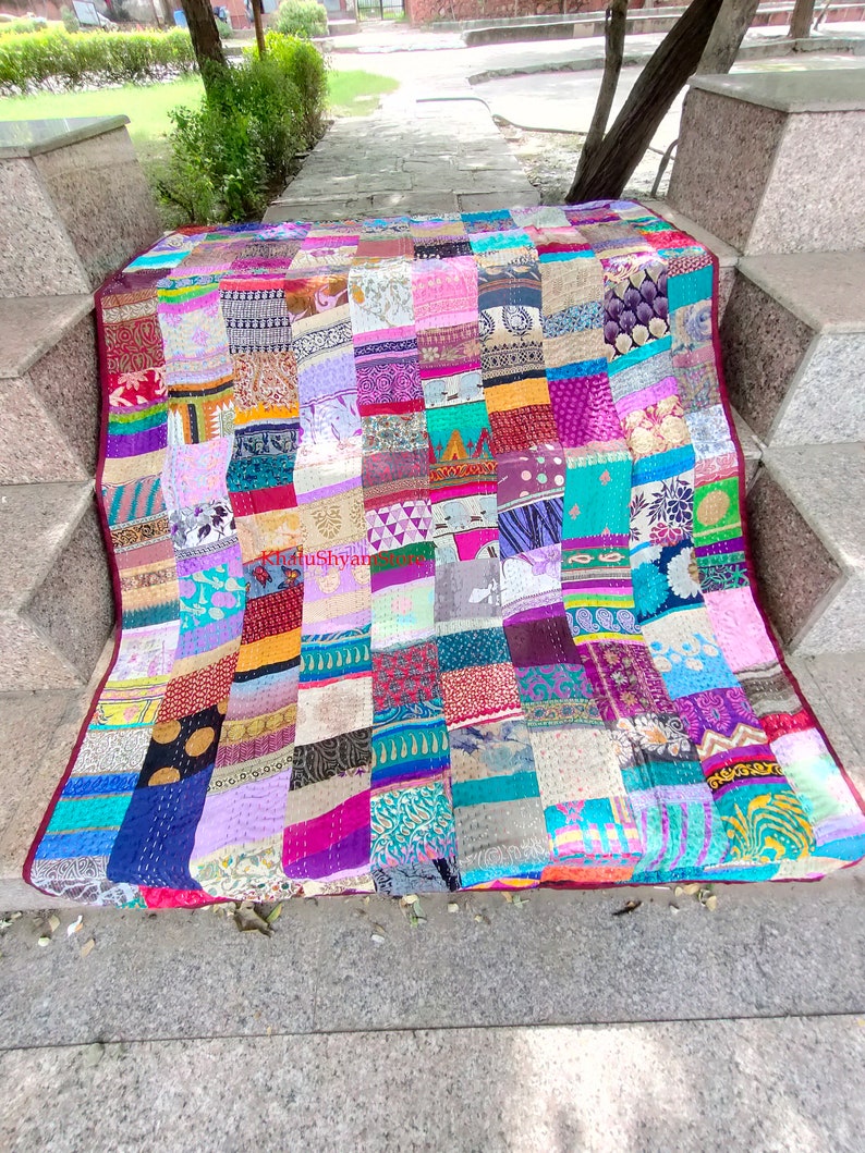 May include: A colorful patchwork quilt made from repurposed fabric scraps. The quilt is made up of squares of different colors and patterns, including floral, paisley, and geometric designs. The quilt is laid out on a set of stone steps.