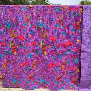 May include: Purple kantha quilt with a floral and bird pattern. The quilt is made of cotton and has a hand-stitched design. The quilt is reversible and has a solid purple color on the back.