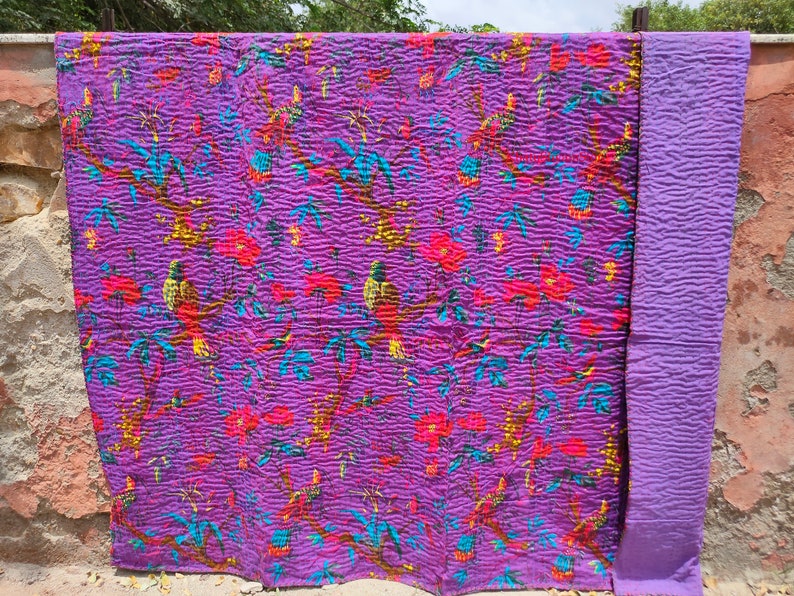 May include: Purple kantha quilt with a floral and bird pattern. The quilt is made of cotton and has a hand-stitched design. The quilt is reversible and has a solid purple color on the back.