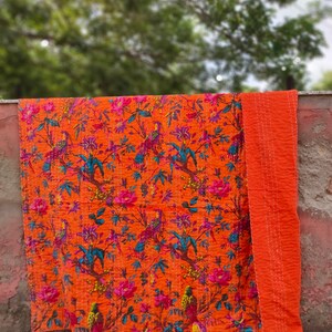 May include: An orange kantha quilt with a floral and bird pattern. The quilt is folded in half and has a solid orange back.