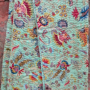 Może przedstawiać: Zielona kołdra kantha z kwiatowym wzorem w odcieniach czerwieni, żółci, błękitu i brązu. Kołdra jest wykonana z bawełny i ma ręcznie szyty wzór.