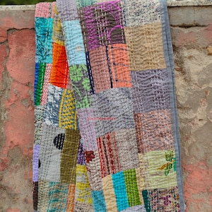 May include: A patchwork quilt made from a variety of colorful fabrics, including floral prints, stripes, and geometric patterns. The quilt is hand-stitched and has a rustic, vintage look.