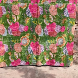 Könnte beinhalten: Eine grüne Kantha-Steppdecke mit einem floralen und Ananas-Muster in Rosa-, Orange- und Weißtönen. Die Steppdecke ist handgenäht und hat einen Vintage-Look.