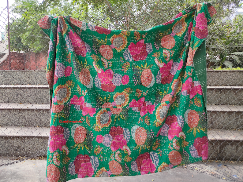 Op de afbeelding: Een groene kantha-deken met een bloemen- en ananaspatroon. De deken is gemaakt van katoen en met de hand gestikt.