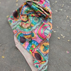 Puede incluir: Una colcha kantha colorida con un patr&oacute;n de paisley. La colcha est&aacute; doblada y tiene un respaldo blanco con costuras rojas.