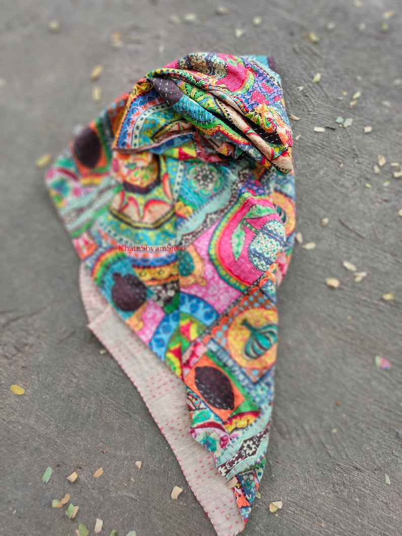 Puede incluir: Una colcha kantha colorida con un patr&oacute;n de paisley. La colcha est&aacute; doblada y tiene un respaldo blanco con costuras rojas.