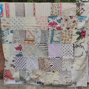 Może przedstawiać: Kołdra patchworkowa wykonana z różnych tkanin o różnych wzorach i kolorach. Kołdra składa się z kwadratów i prostokątów, a tkaniny są zszyte ze sobą, tworząc unikalny i interesujący wzór. Kołdra jest pięknym przykładem rękodzieła.