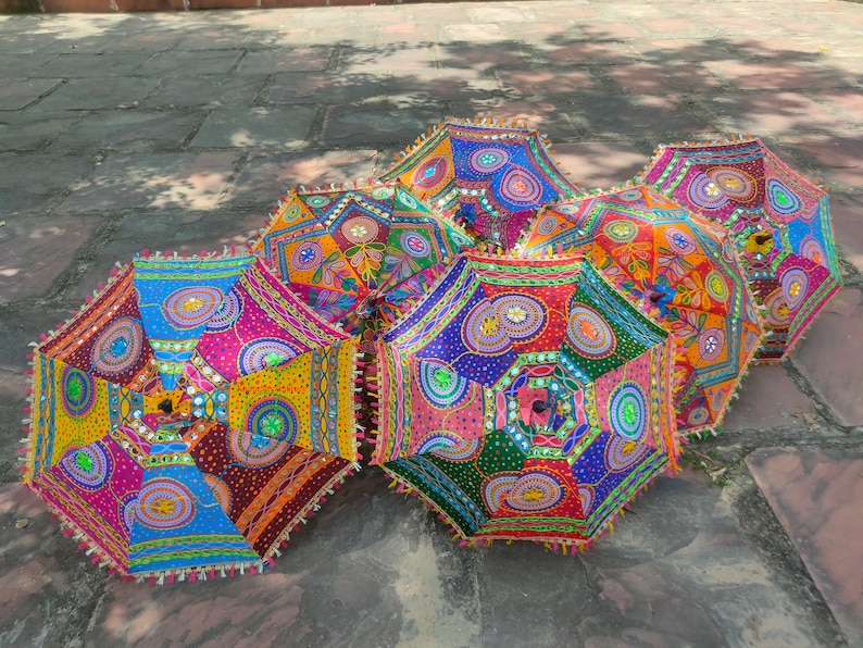 May include: Five colorful umbrellas with intricate embroidery and mirror embellishments. The umbrellas are made of fabric and have a traditional Indian design.