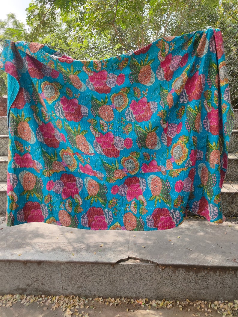 Op de afbeelding: Een turquoise blauwe kantha-deken met een bloemen- en ananaspatroon. De deken is gemaakt van katoen en heeft een handgestikt ontwerp.