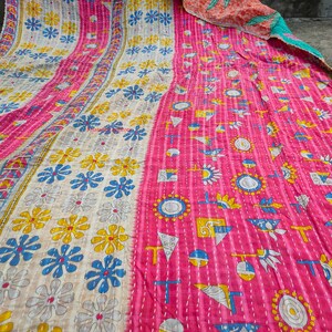 May include: A vibrant, handmade quilt with a patchwork design. The quilt features a pink and cream color scheme with floral and geometric patterns in yellow, blue, and white. The quilt is made of soft fabric and has visible stitching.