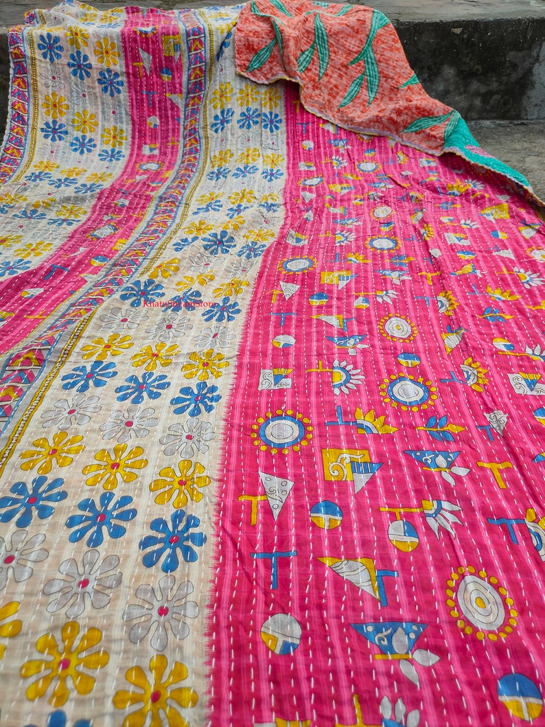 May include: A vibrant, handmade quilt with a patchwork design. The quilt features a pink and cream color scheme with floral and geometric patterns in yellow, blue, and white. The quilt is made of soft fabric and has visible stitching.