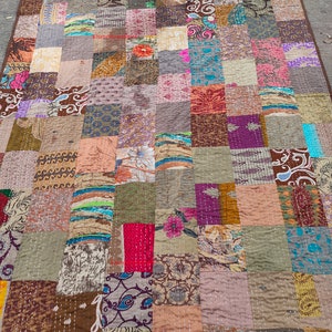 Könnte beinhalten: Eine Patchwork-Decke mit einer Vielzahl von Farben und Mustern, darunter Braun, Beige, Rosa, Blau und Grün. Die Decke besteht aus vielen verschiedenen Stoffen, die in einem Gittermuster zusammengenäht sind.