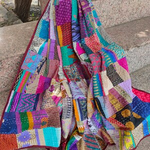 May include: A colorful patchwork quilt made from repurposed fabrics. The quilt is made up of squares and rectangles of different colors and patterns, including floral prints, paisley designs, and stripes. The quilt is hand-stitched and has a unique, vintage look.