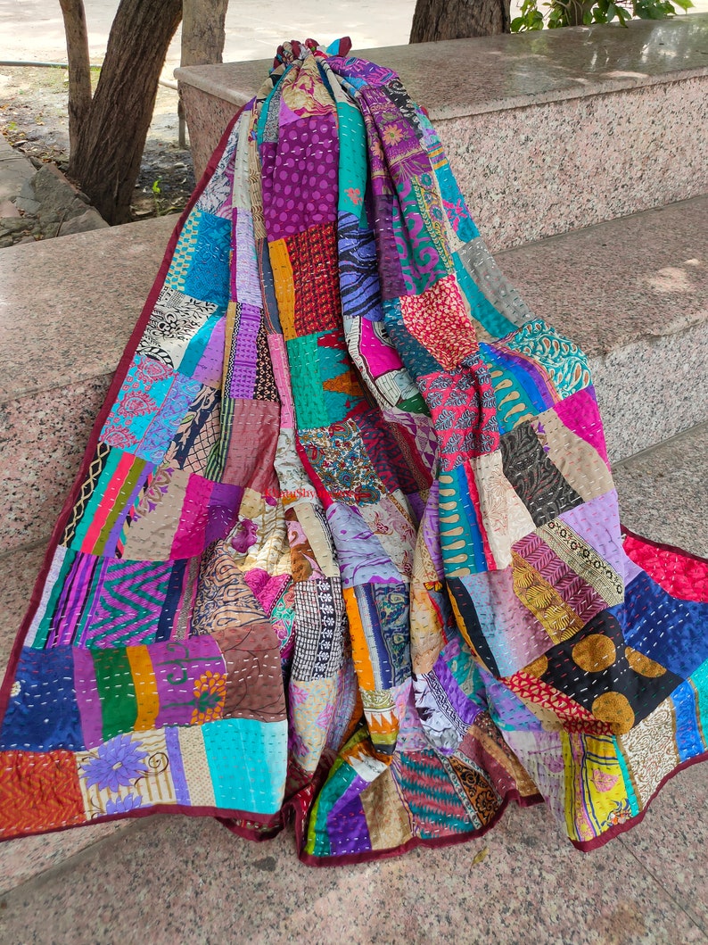 May include: A colorful patchwork quilt made from repurposed fabrics. The quilt is made up of squares and rectangles of different colors and patterns, including floral prints, paisley designs, and stripes. The quilt is hand-stitched and has a unique, vintage look.