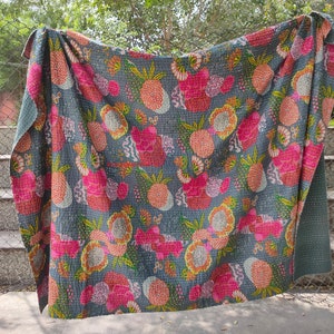 Op de afbeelding: Een grijs kantha-dekbed met een bloemen- en ananaspatroon in tinten roze, geel en groen. Het dekbed is gemaakt van katoen en met de hand gestikt.