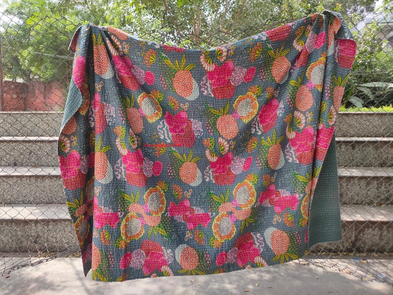 Op de afbeelding: Een grijs kantha-dekbed met een bloemen- en ananaspatroon in tinten roze, geel en groen. Het dekbed is gemaakt van katoen en met de hand gestikt.