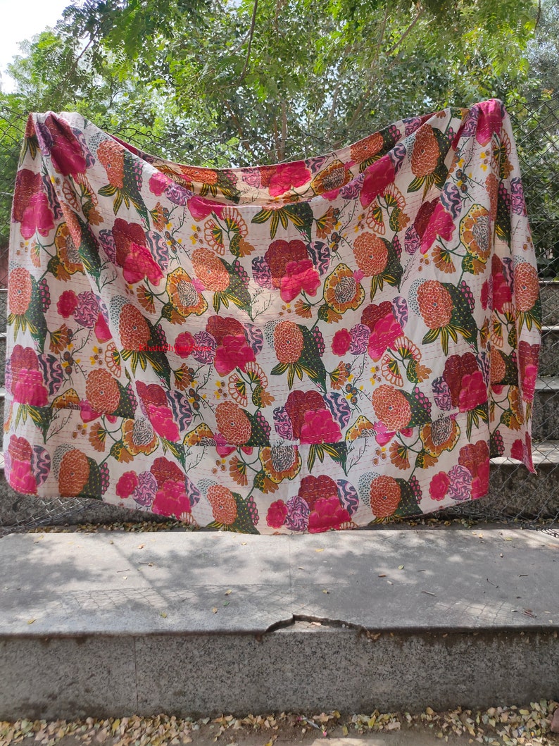 Op de afbeelding: Een wit kantha-dekbed met een bloemenpatroon in tinten roze, oranje en groen. Het dekbed is gemaakt van katoen en met de hand gestikt.