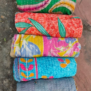 May include: Five rolled, colorful, quilted fabric pieces. The top piece is green with a floral pattern, followed by orange with leaves, then pink and yellow, blue with a floral design, and finally, a gray piece with embroidered flowers.