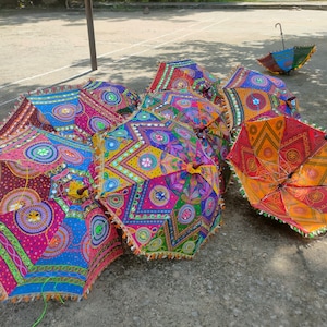 May include: A group of colorful, patterned umbrellas with intricate embroidery and mirror embellishments. The umbrellas are arranged on a gray, textured surface.