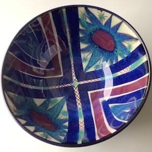 May include: A blue and white ceramic bowl with a geometric design. The bowl has a white background with blue and purple geometric shapes and a blue rim.