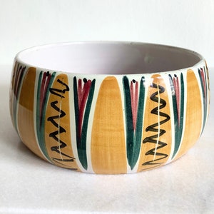May include: A yellow ceramic bowl with a white interior and a colourful geometric design. The design features green, red and brown lines and zigzags.