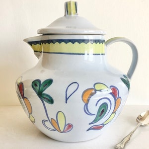 May include: White ceramic jug with a lid and a handle. The jug has a yellow, blue and green floral design.