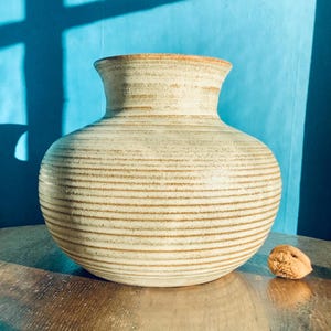 May include: A large, white ceramic vase with brown stripes. The vase has a rounded body and a wide mouth.