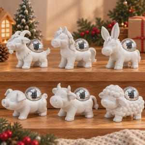 Puede incluir: Un conjunto de seis figuras de animales blancas que incluyen una cabra, un caballo, un burro, un cerdo, una vaca y una oveja. Cada figura presenta una pequeña bola de discoteca plateada y reflectante fijada en su espalda.