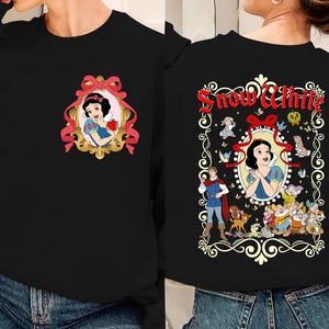May include: Black sweatshirt with a white graphic print of Snow White and the Seven Dwarfs. The graphic features Snow White in a mirror frame with the text "Snow White" above her. The graphic also includes the Seven Dwarfs, a deer, and a bird.