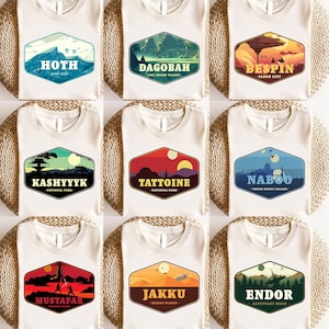 May include: Nine different Star Wars themed t-shirts featuring various planets and locations from the movies. Each t-shirt has a unique design with a vintage national park style logo. The planets featured are Hoth, Dagobah, Bespin, Kashyyyk, Tatooine, Naboo, Mustafar, Jakku, and Endor.