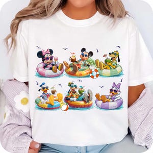 May include: White t-shirt featuring a colorful graphic of Disney characters relaxing in inner tubes. Minnie Mouse, Mickey Mouse, Goofy, Donald Duck, Pluto, and Daisy Duck are depicted enjoying tropical drinks and ice cream.