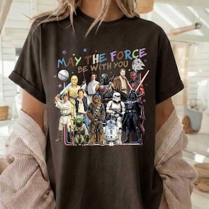 以下が含まれることがあります： ダース・ベイダー、ヨーダ、R2-D2など、スター・ウォーズのキャラクターが描かれた、ダークブラウンのTシャツ。キャラクターの上には「MAY THE FORCE BE WITH YOU」の文字。半袖でクルーネックです。