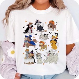 Op de afbeelding: Een wit t-shirt met een grafische print van diverse cartoonhonden in Halloween-kostuums, waaronder mummies, heksen en vampiers, omringd door kleine illustraties van vleermuizen en candy corn in het midden van het kledingstuk.