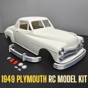 May include: A white 1949 Plymouth RC model kit. The kit includes the car body, front bumper, and several small parts. The model has a classic car design with a rounded roof and prominent front grille. The text "1949 Plymouth RC Model Kit" is displayed at the bottom.