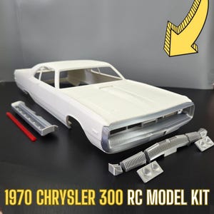 May include: A white 1970 Chrysler 300 RC model car kit. The kit includes the car body, a chrome grille, and other parts. The car is a classic American muscle car.