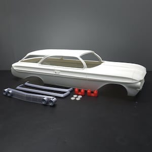 May include: A white plastic model car body with separate gray and red components. The car body is a classic coupe shape. Additional parts include a grill, trim pieces, and small red and white pieces.