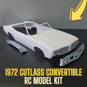 May include: A white plastic model kit of a 1972 Cutlass Convertible RC car. The kit includes the body, chassis, and front bumper. The car is in a disassembled state.