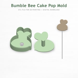 以下が含まれることがあります： 「Bumble Bee Cake Pop Mold」と「STL FILE FOR 3D PRINTING - DIGITAL DOWNLOAD」の文字が入った、薄緑色のハチのケーキポップ型。型は2つのパーツで構成されており、下部には小さな穴があります。