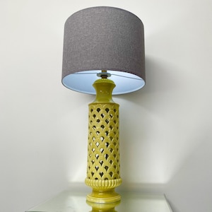 May include: A decorative table lamp with a grey fabric shade. The lamp base is a yellow-green colour with a cut-out pattern. The lamp is approximately 76 cm tall.