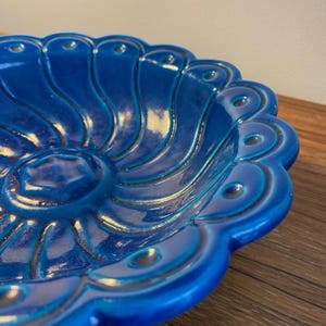 May include: A large, blue ceramic bowl with a scalloped edge and a swirling, textured design. The bowl is glazed in a deep, rich blue colour.