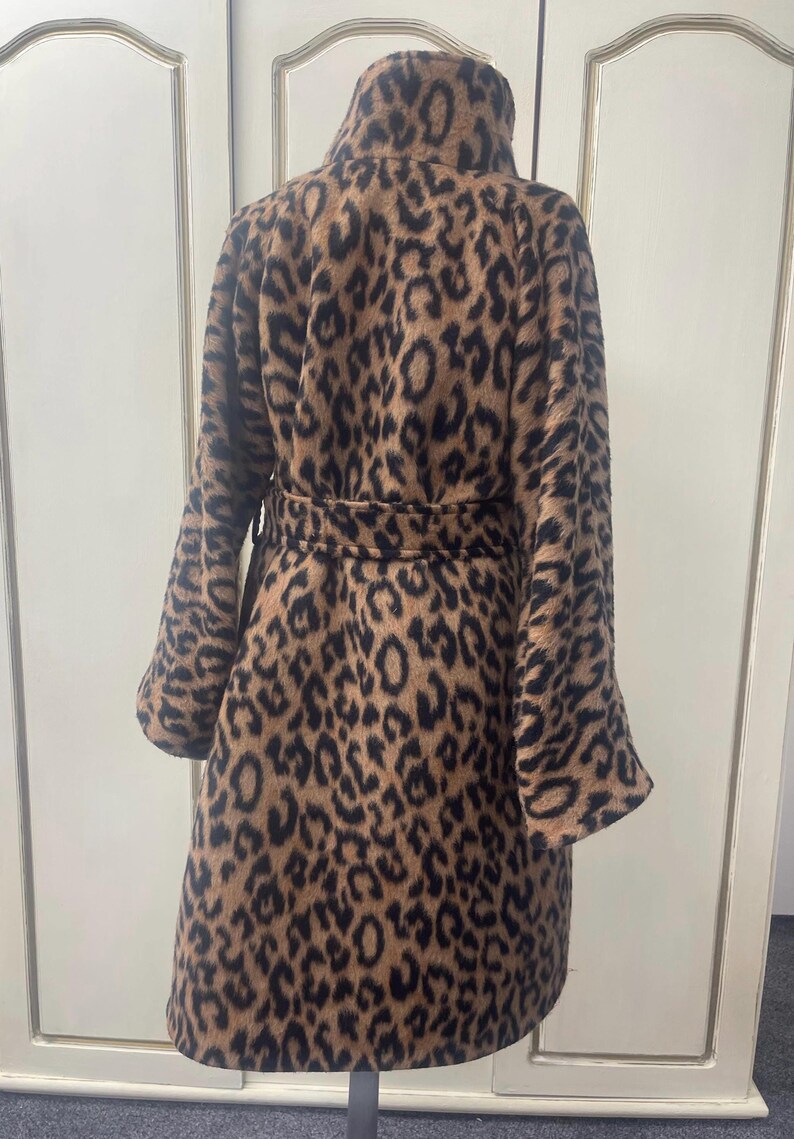 May include: A brown and black leopard print coat with a high collar and a belt. The coat has long sleeves and a fitted silhouette.