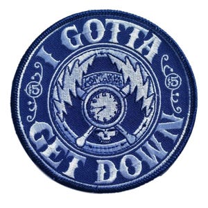 Puede incluir: Parche redondo azul marino con texto blanco bordado: "I GOTTA GET DOWN". El diseño central presenta un reloj, rayos y la palabra "Fantasia".