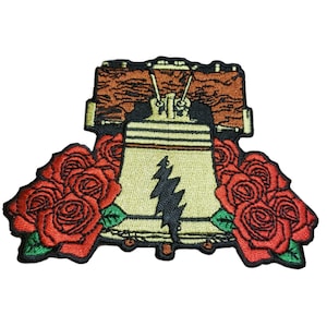Può includere: Toppa ricamata raffigurante una Liberty Bell stilizzata con un fulmine nero. La campana è affiancata da rose rosse con foglie verdi. La parte superiore della toppa presenta un design in legno marrone.