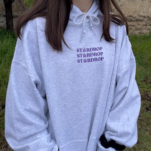 May include: A grey hooded sweatshirt with the text "Stardrop" repeated three times in purple lettering.