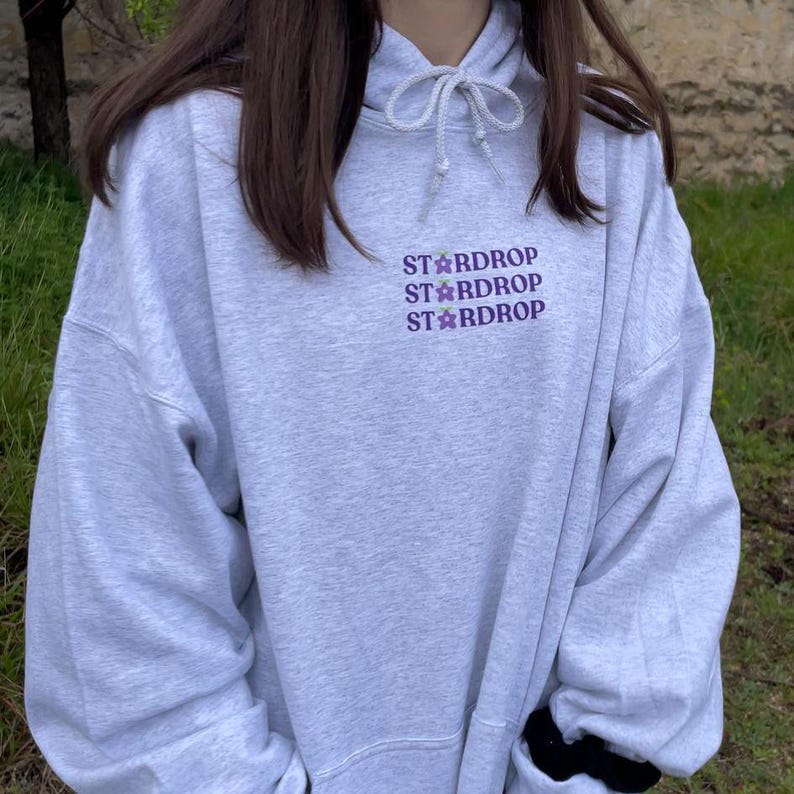 May include: A grey hooded sweatshirt with the text "Stardrop" repeated three times in purple lettering.