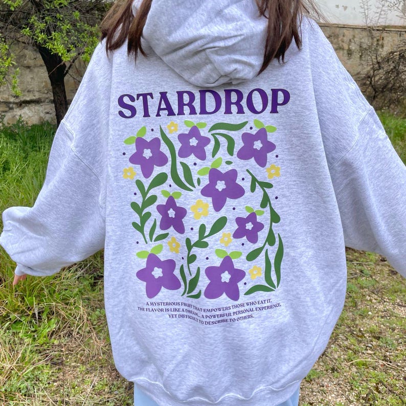 May include: Grey hooded sweatshirt with a purple and green floral design and the text "STARDROP" in purple. The text below the design reads "A mysterious fruit that empowers those who eat it. The flavour is like a dream... a powerful personal experience, yet difficult to describe to others."