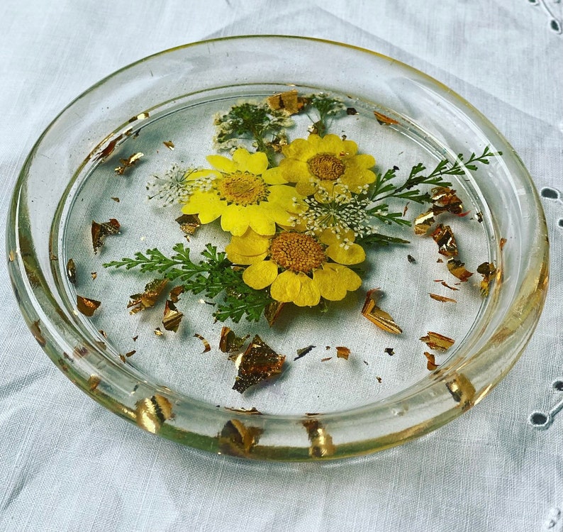 May include: A clear glass coaster with a resin design of yellow flowers and gold leaf accents.