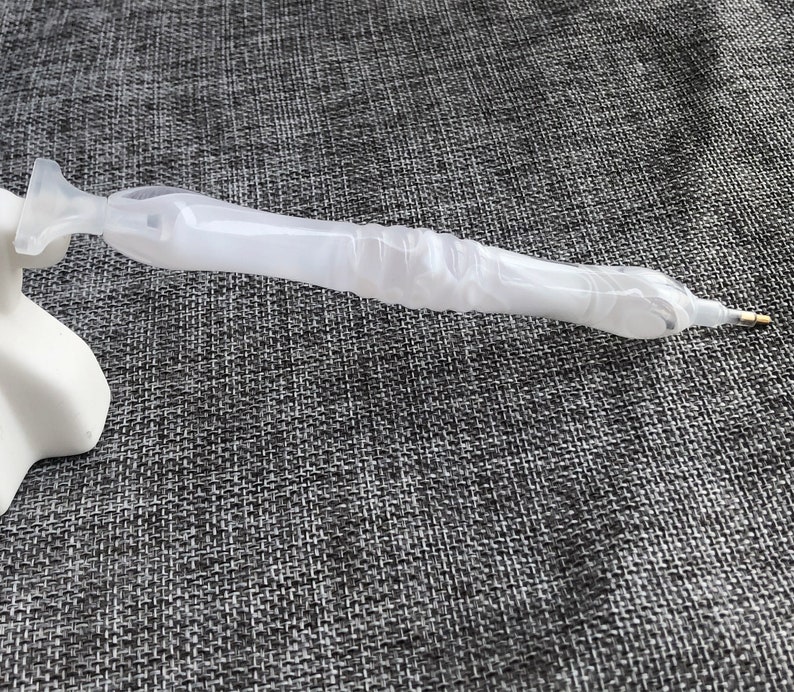 May include: A white diamond painting pen with a clear plastic barrel and a gold tip.